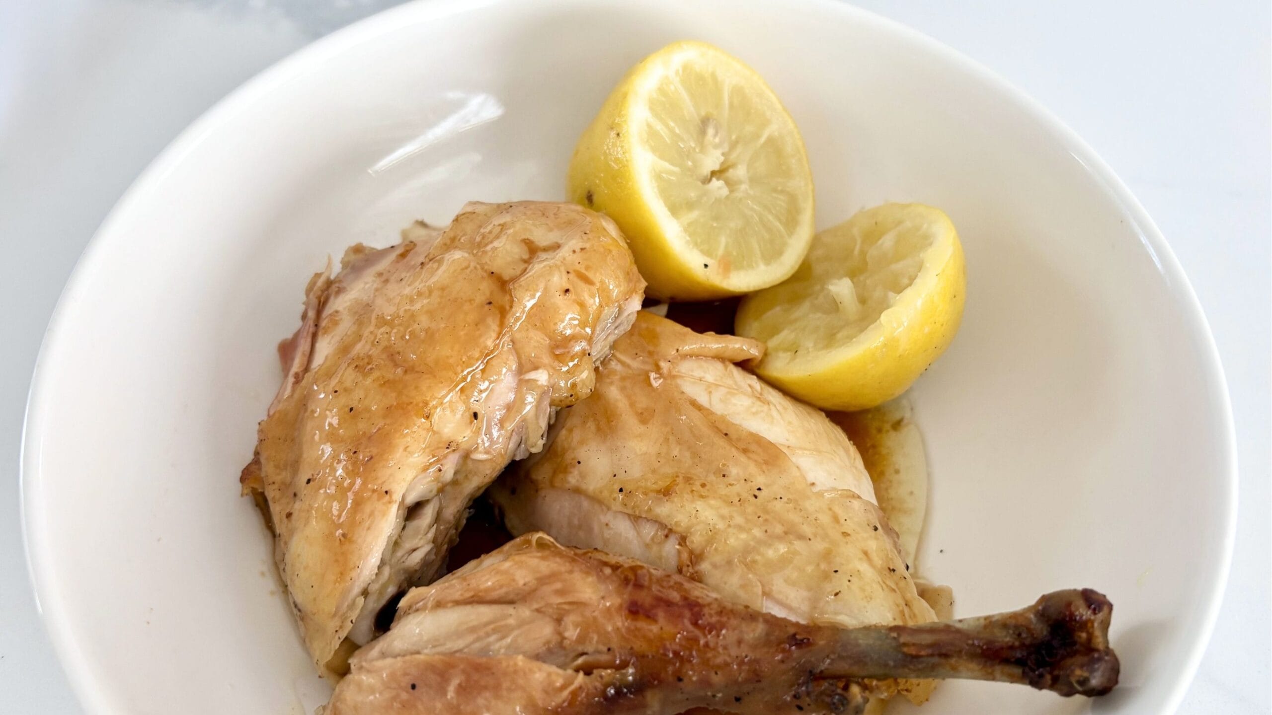 Close up of roast chicken with lemons showing crispy golden skin and juicy meat.