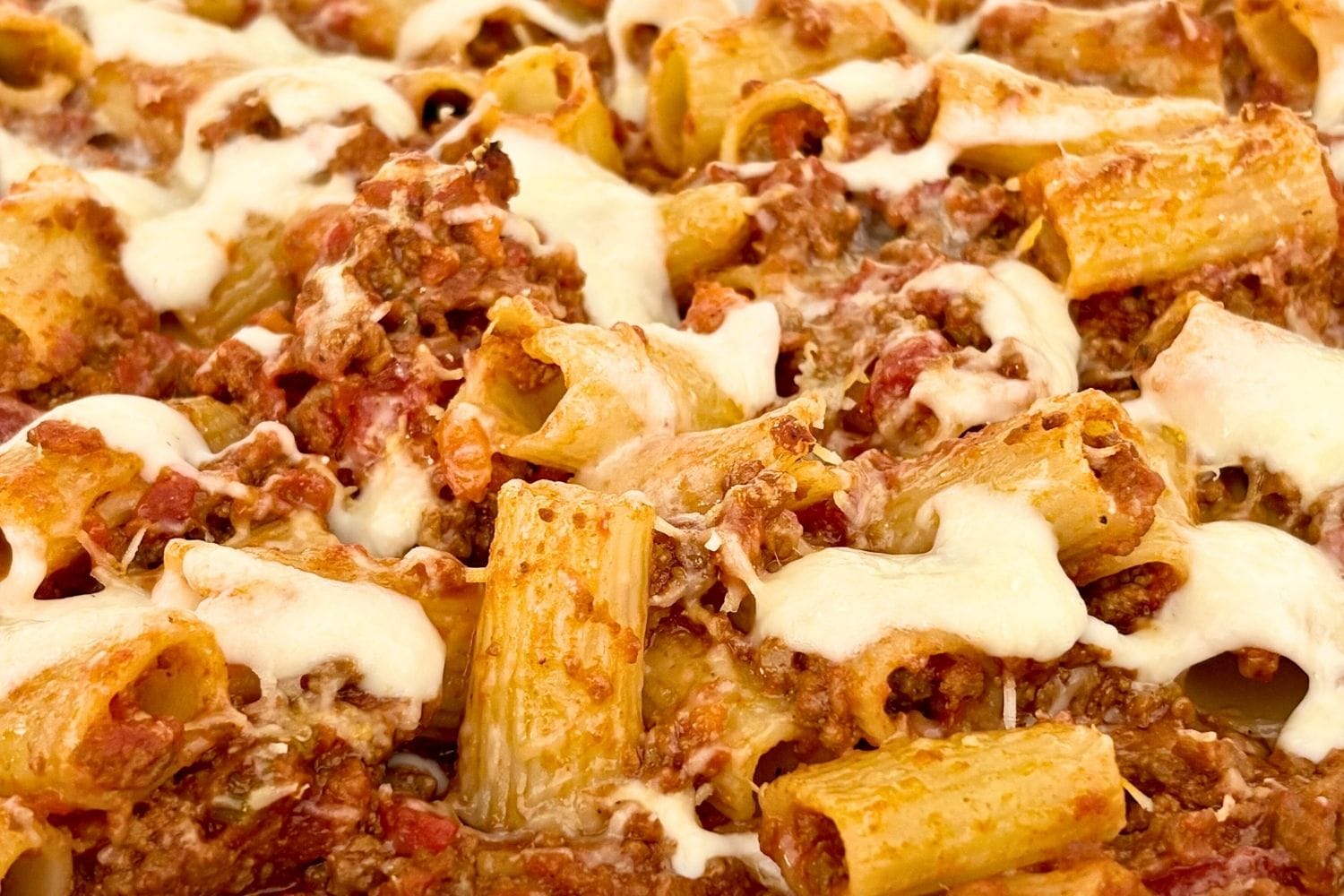 Close-up of baked rigatoni with Bolognese and melted cheese in a baking dish.