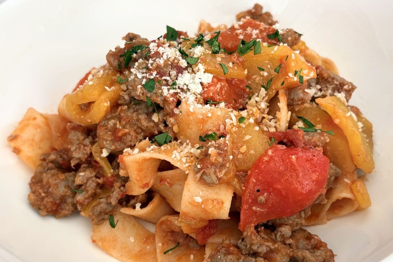 Close-up of sausage and bell pepper pasta with tomatoes and grated cheese