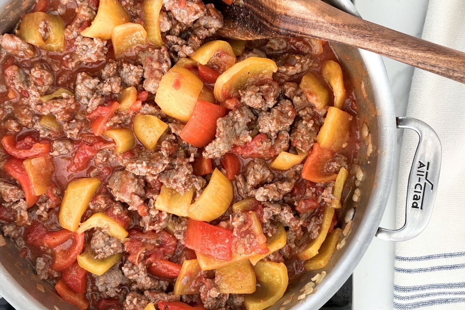 Sausage and bell pepper tomato sauce cooking in a pan with wooden spoon