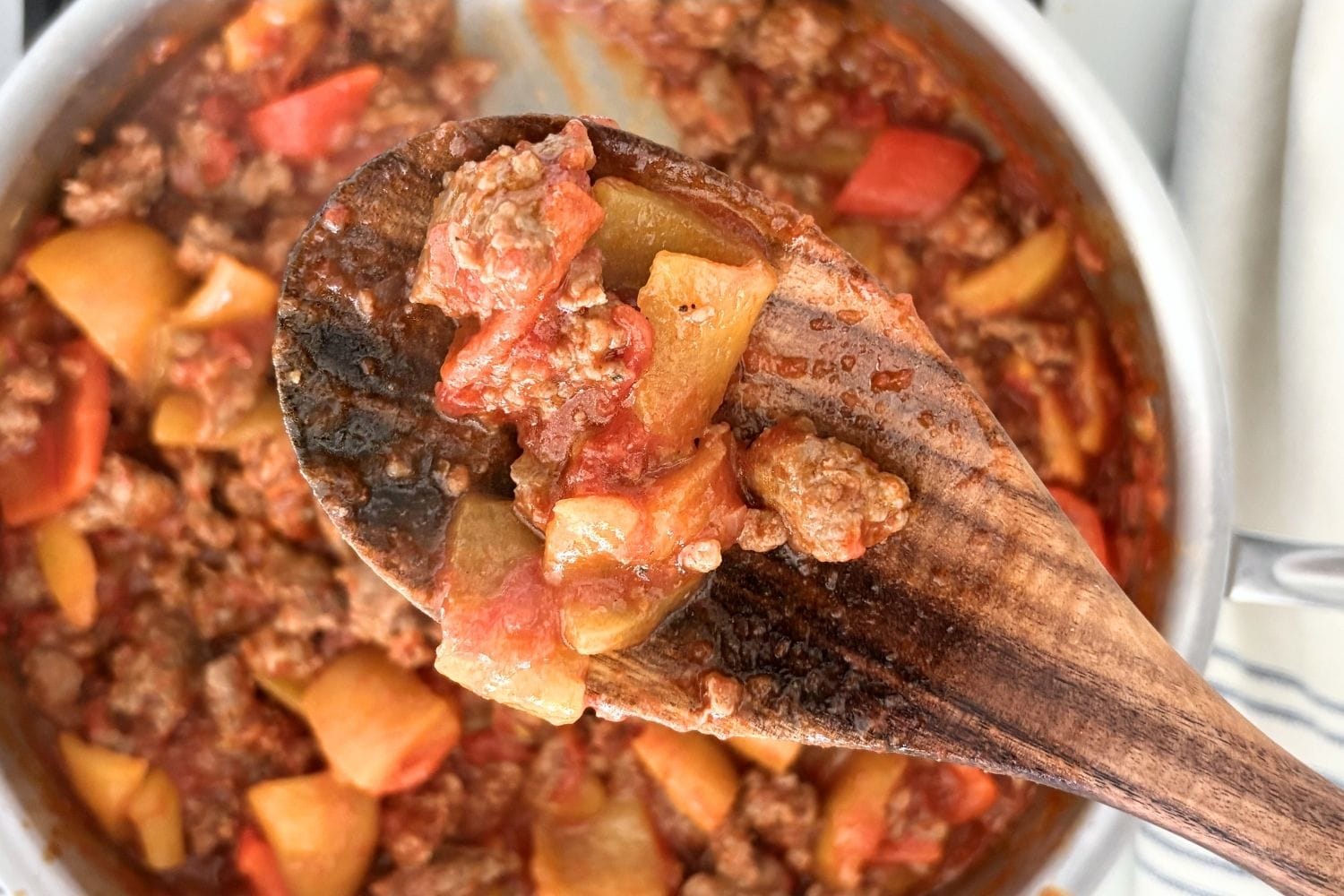 Close-up of sausage and bell pepper tomato sauce on a wooden spoon over the pan