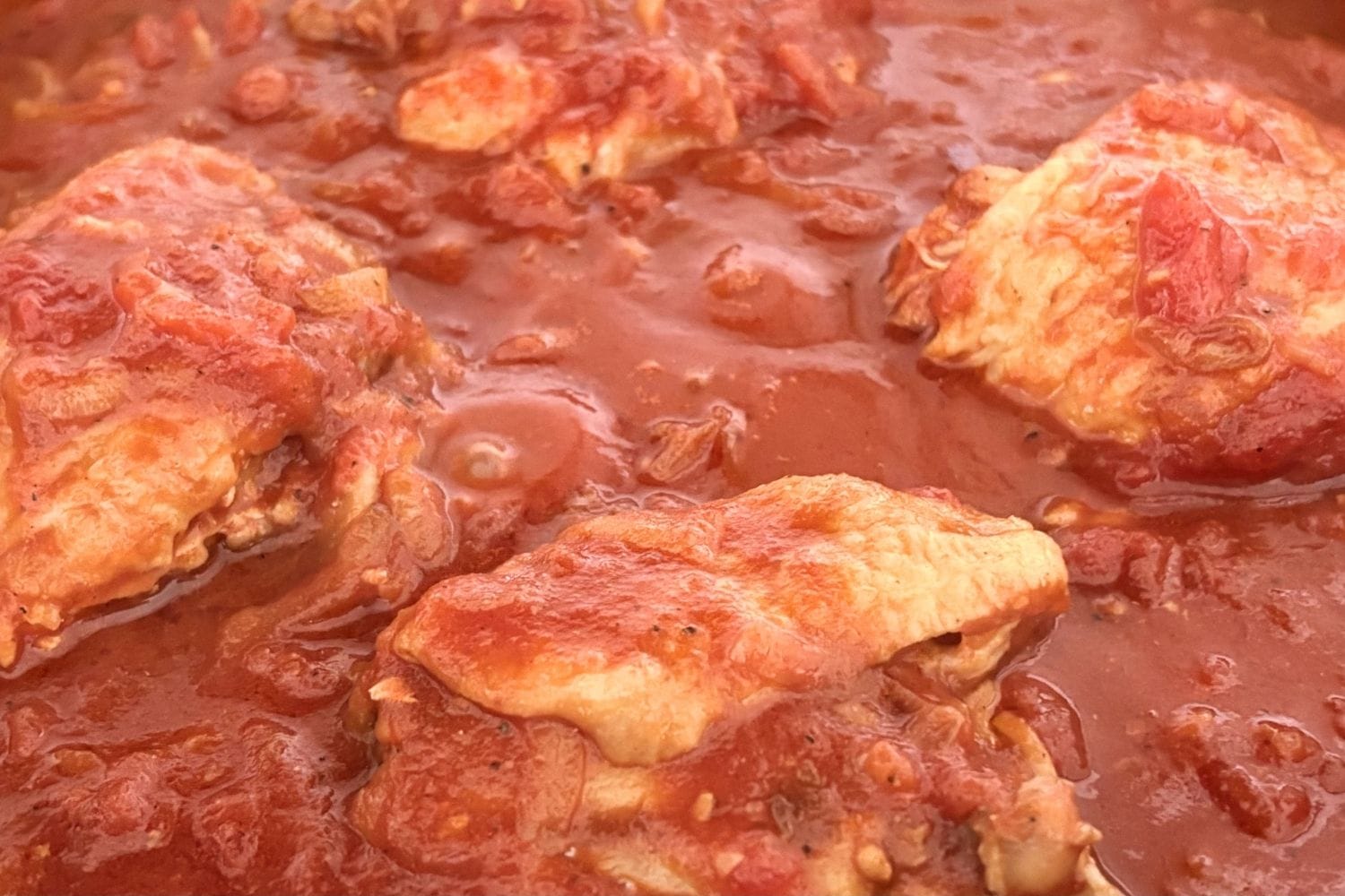Chicken cacciatore simmering in tomato sauce with bone in chicken thighs, sliced onion, and garlic cooked until tender
