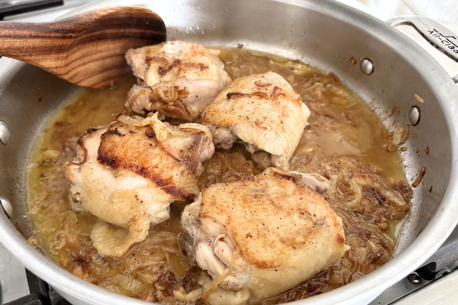 Chicken thighs browning in olive oil with thinly sliced onions, deglazed with white wine in a sauté pan