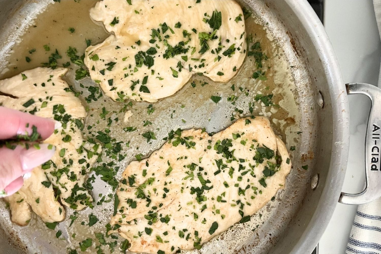 Chicken breast fillets in a stainless steel skillet finished with lemon sauce and fresh parsley.