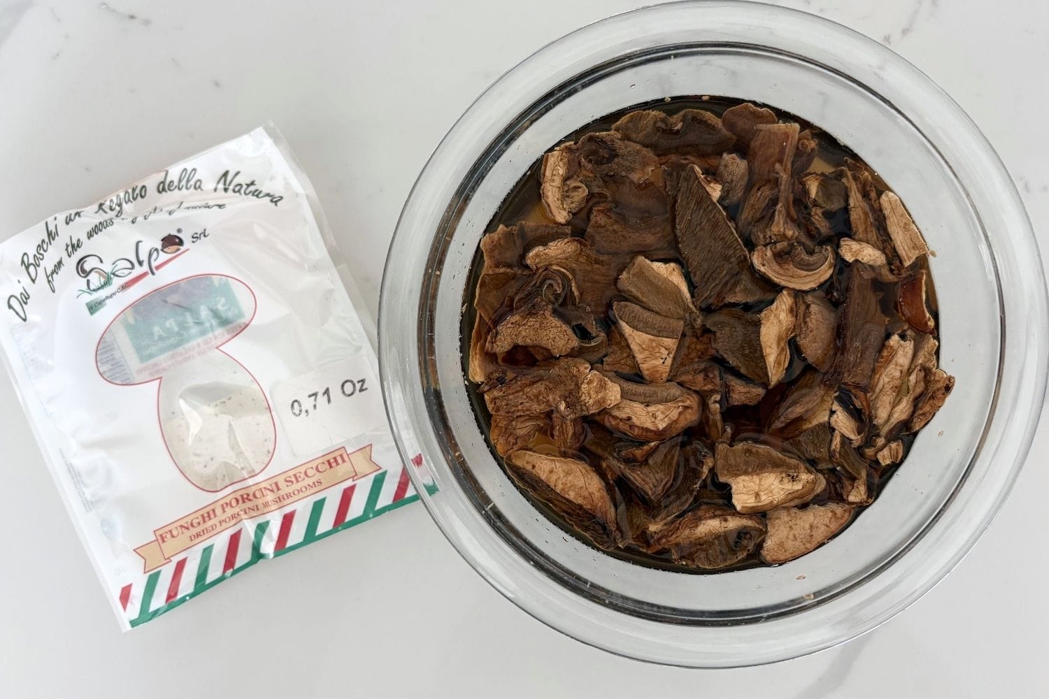 Dried porcini mushrooms soaking in water with package shown before reconstitution