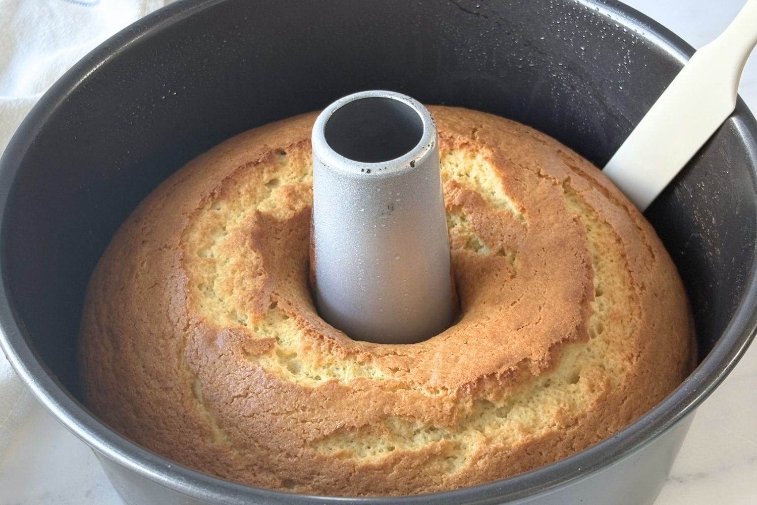 Freshly baked olive oil cake in a tube pan with a golden cracked top cooling after baking.