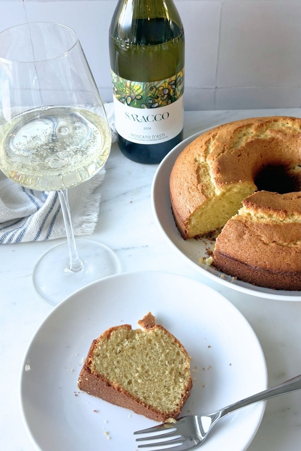 Slice of olive oil cake served with Moscato d’Asti and full cake in background.