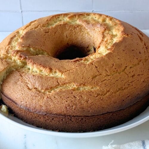 Whole olive oil cake on white platter with one slice removed showing tender crumb.