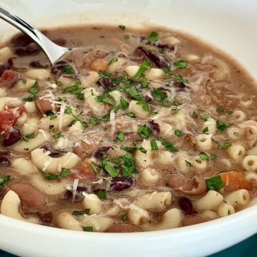 Pasta e fagioli soup with beans, small pasta, parsley, and grated cheese in a white bowl