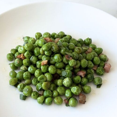 White bowl filled with sautéed peas with pancetta, olive oil, and parsley.