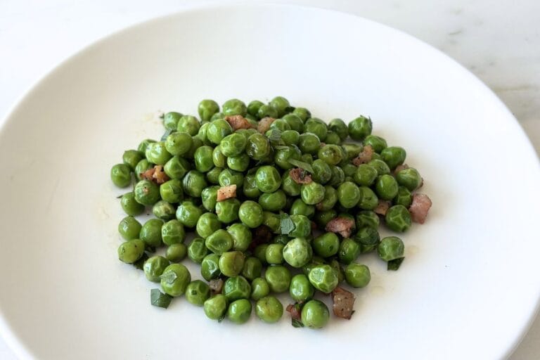 White bowl filled with sautéed peas with pancetta, olive oil, and parsley.