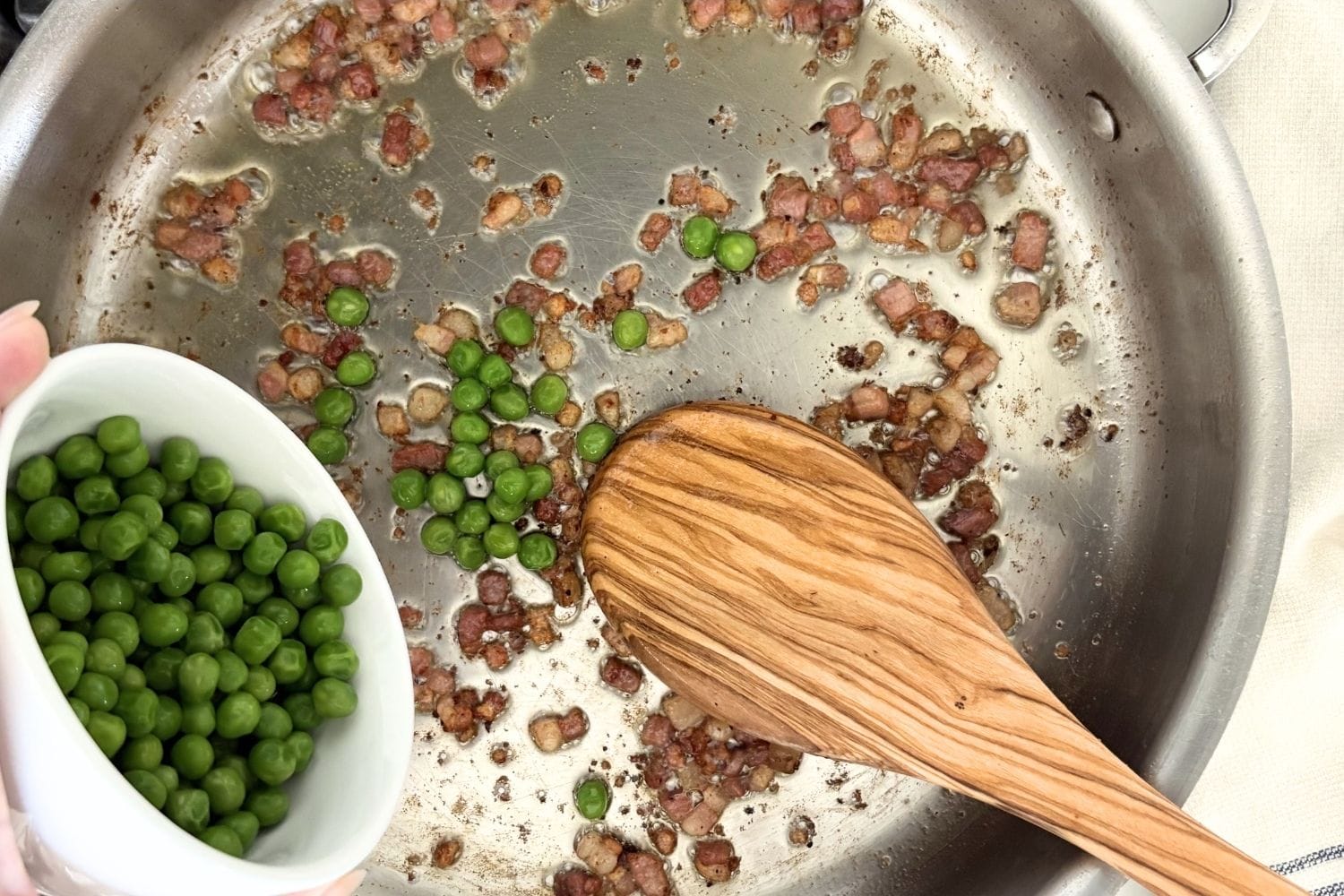 Frozen peas being added to a skillet with crisp pancetta and olive oil.