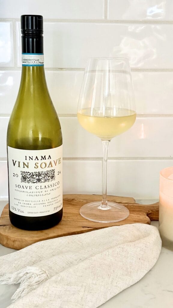 Bottle of Soave Classico Italian white wine with a glass of white wine on a wooden board in a bright kitchen setting.