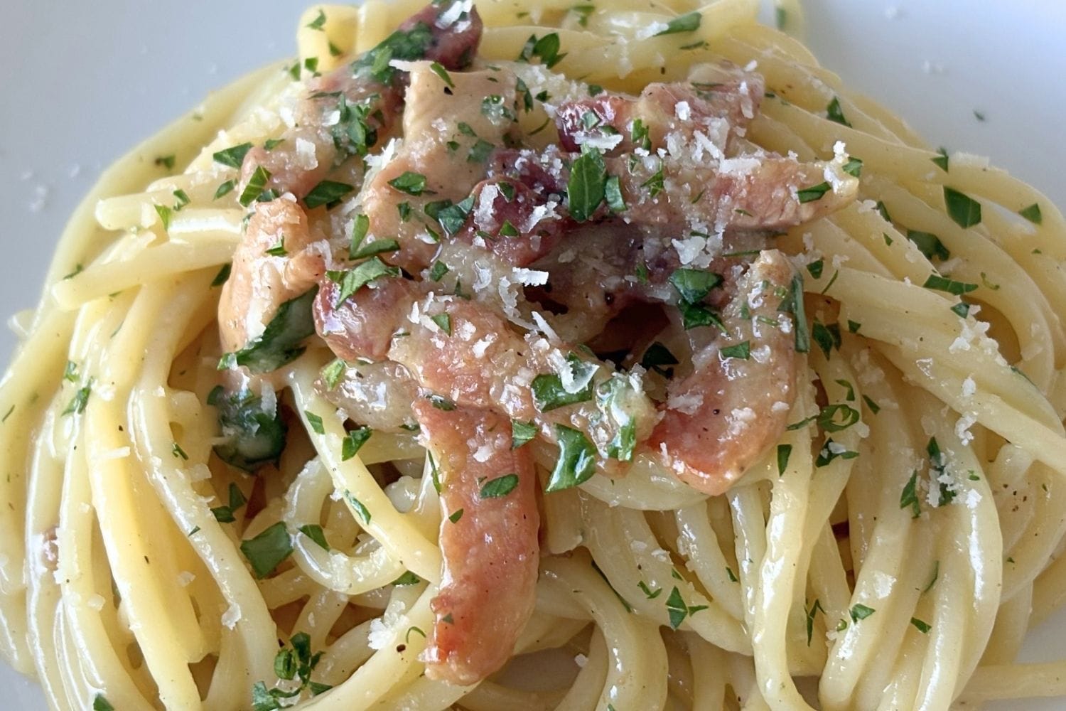 Close-up of Marcella Hazan’s carbonara sauce with spaghetti coated in a glossy egg and cheese sauce, topped with crisp pancetta, parsley, black pepper, and grated cheese.