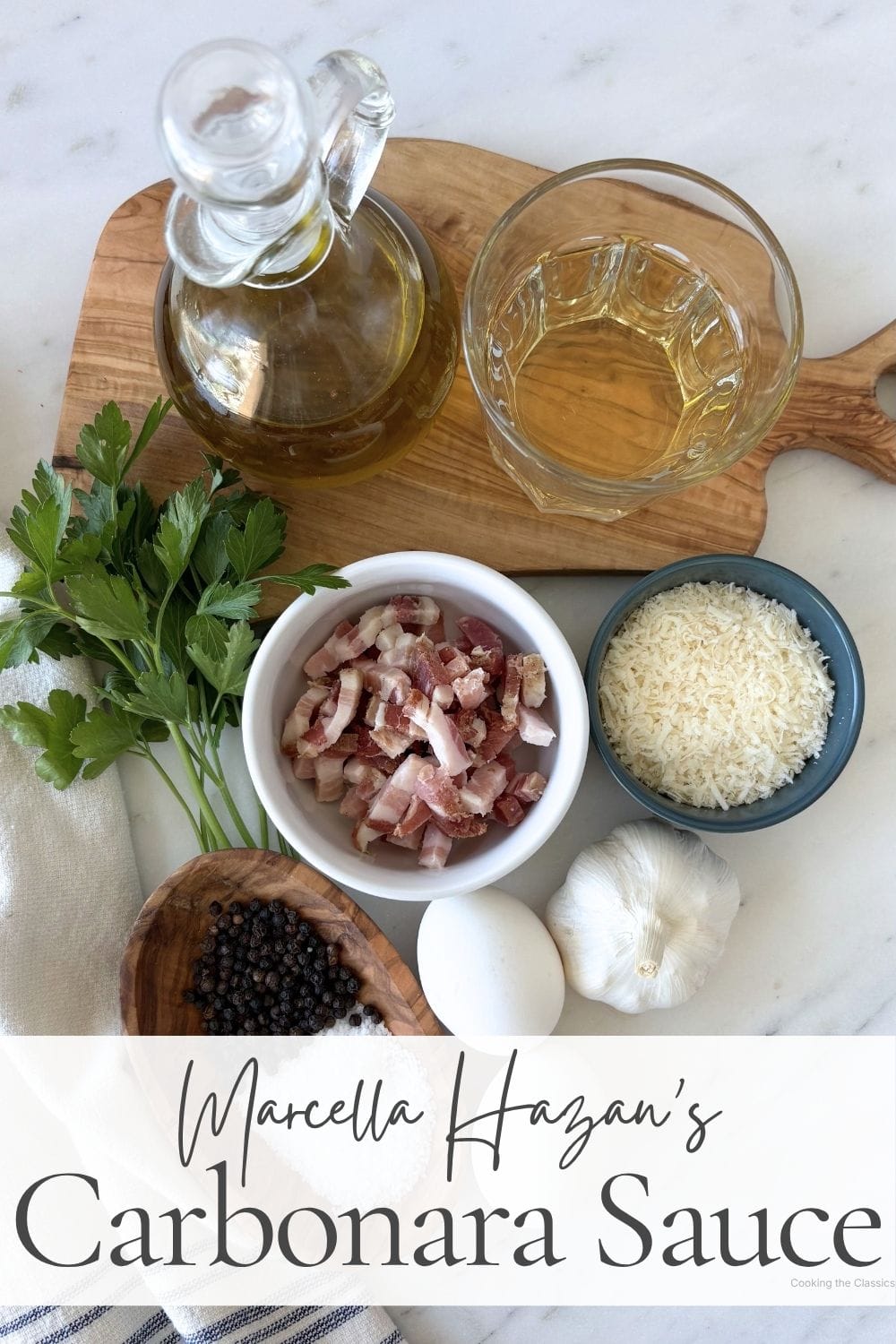 Flatlay of ingredients for Marcella Hazan’s carbonara sauce including pancetta, eggs, garlic, parsley, black pepper, olive oil, grated cheese, and white wine.