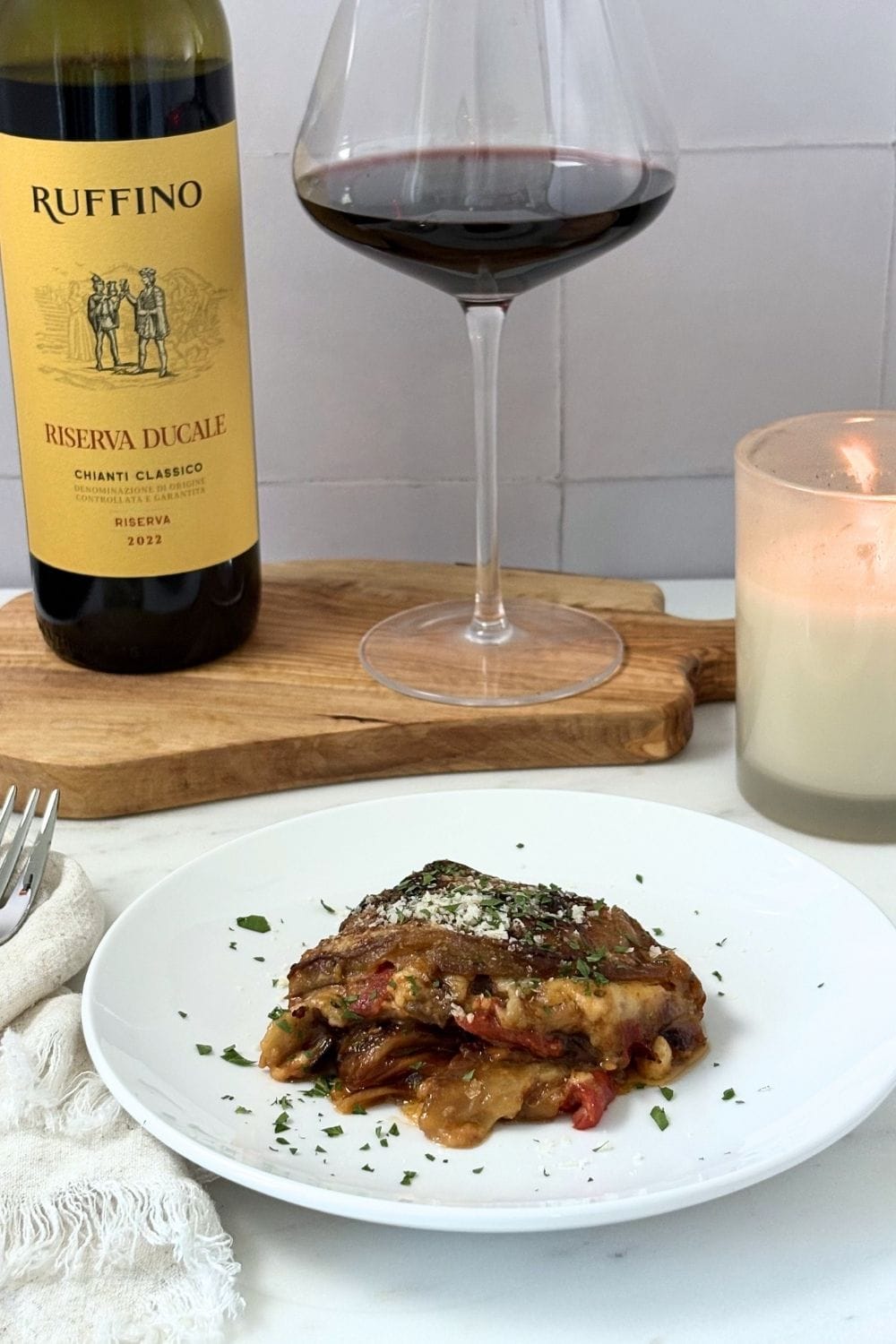 Eggplant Parmesan served with Chianti wine on a marble countertop with candlelight.