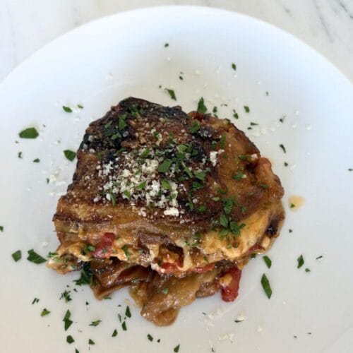 Plate of homemade Eggplant Parmesan topped with parmesan and parsley on a white plate.