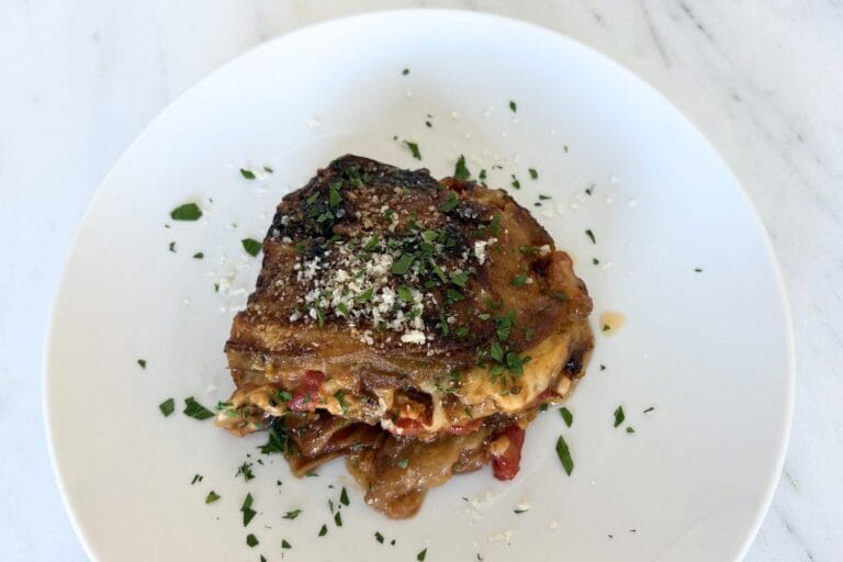Plate of homemade Eggplant Parmesan topped with parmesan and parsley on a white plate.