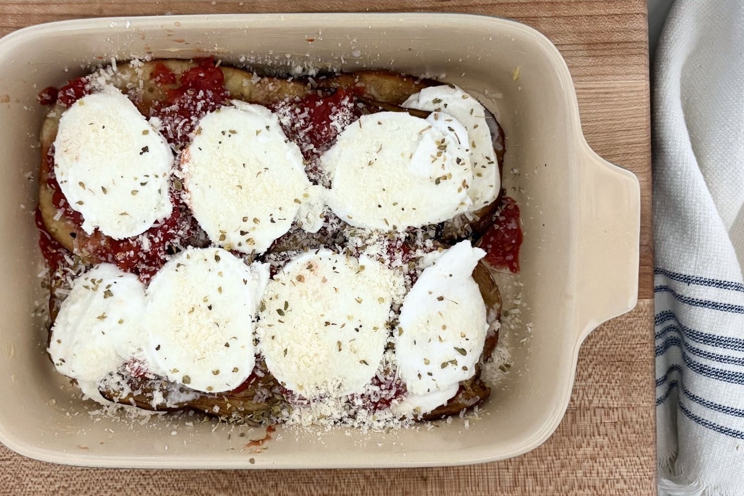 Layered Eggplant Parmesan before baking with fried eggplant, tomatoes, buffalo mozzarella, parmesan, and oregano.