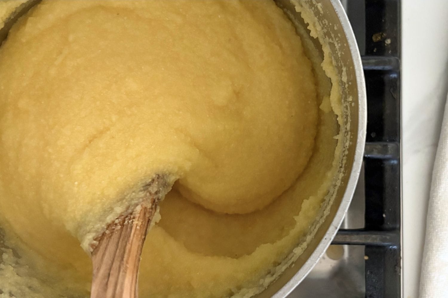 Soft polenta cooking in a pot with a wooden spoon on the stovetop