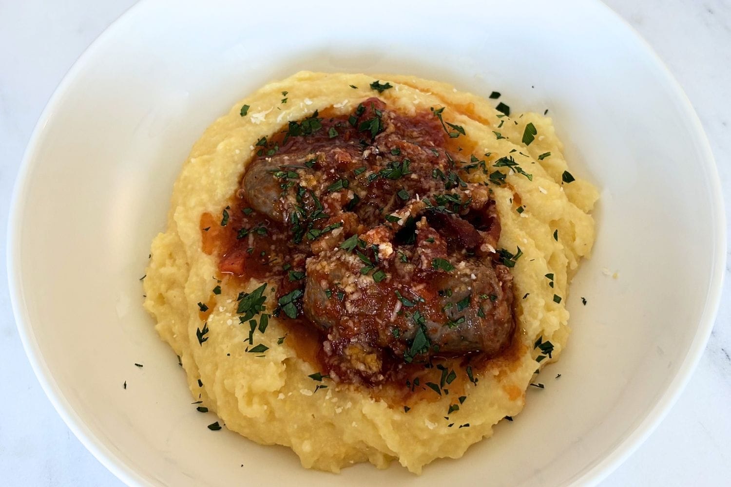 Soft polenta served with Italian sausage in tomato sauce and finished with parsley