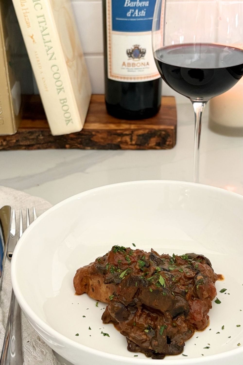 Braised pork chops with porcini and tomato cream sauce served on a white plate with a glass of red wine