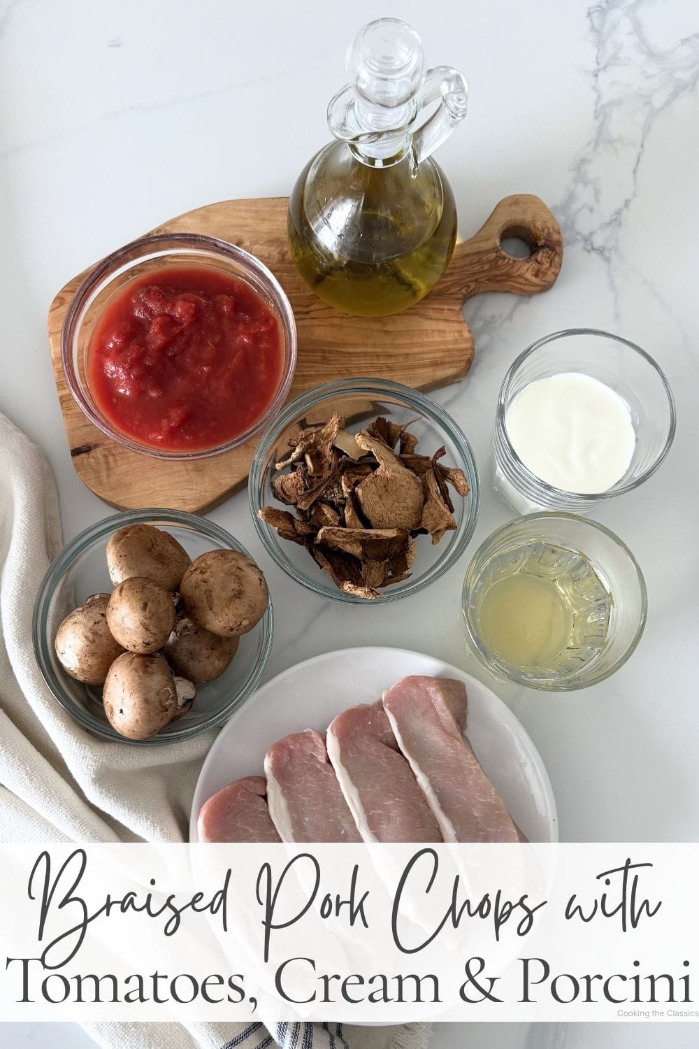 Ingredients for braised pork chops with tomatoes, cream, and porcini mushrooms arranged on a marble surface