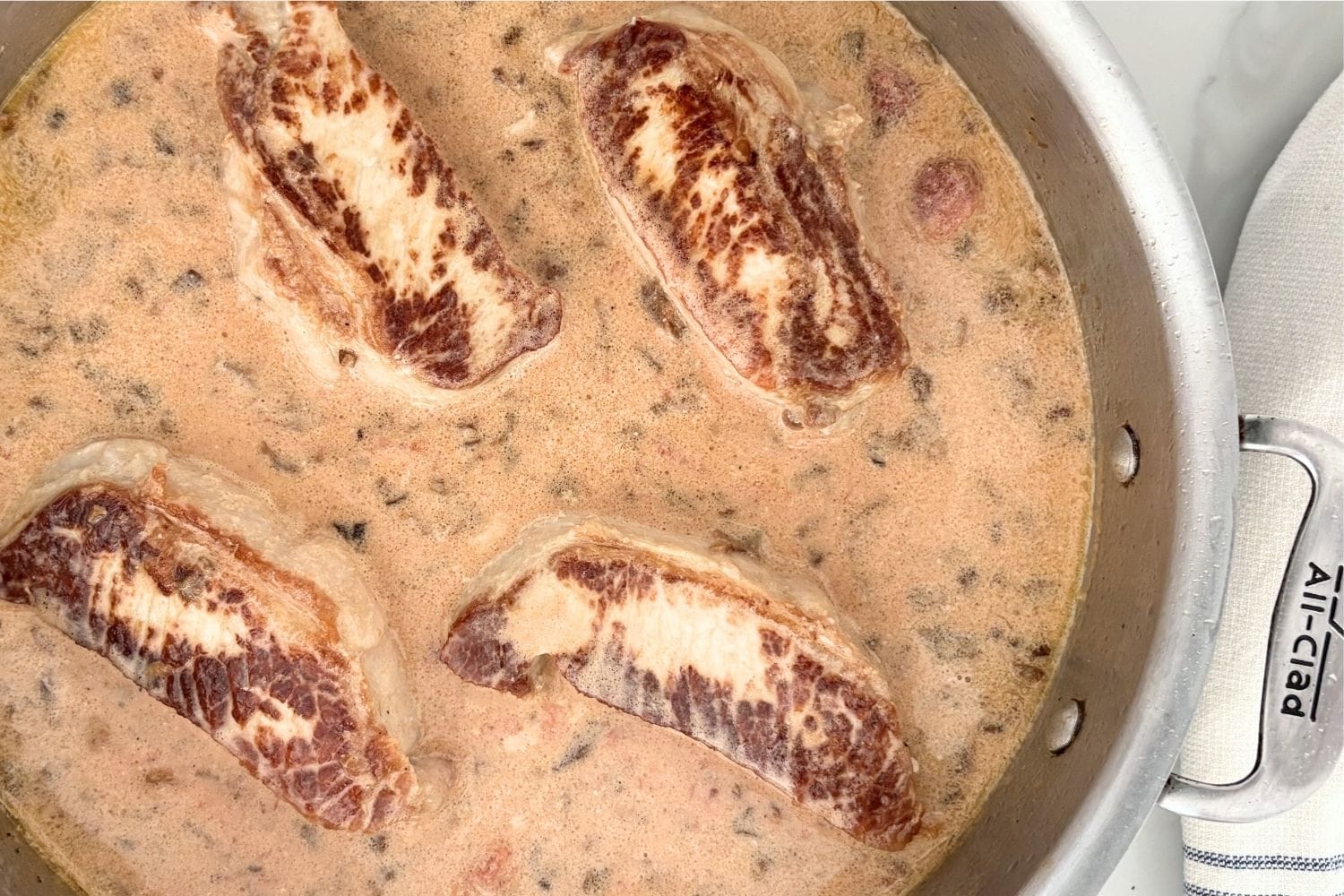Pork chops simmering in a tomato, cream, and porcini sauce in a sauté pan