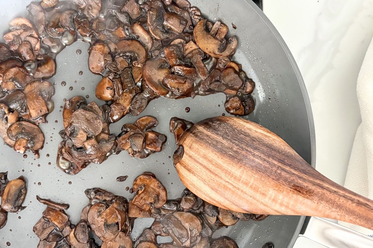 Sliced mushrooms cooking in a pan with a wooden spoon