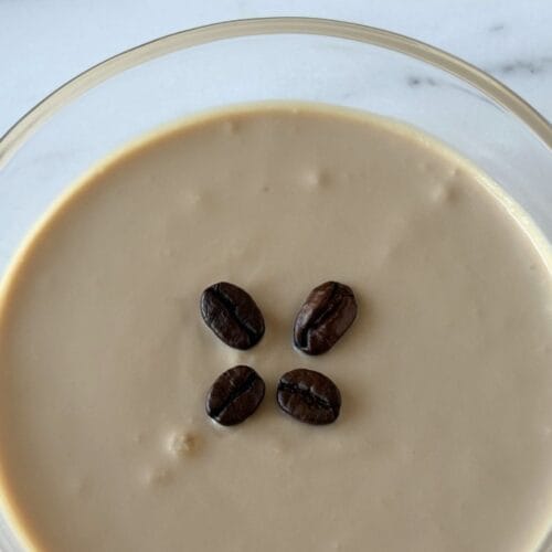 Close-up of ricotta and coffee cream dessert garnished with coffee beans in a shallow glass bowl.