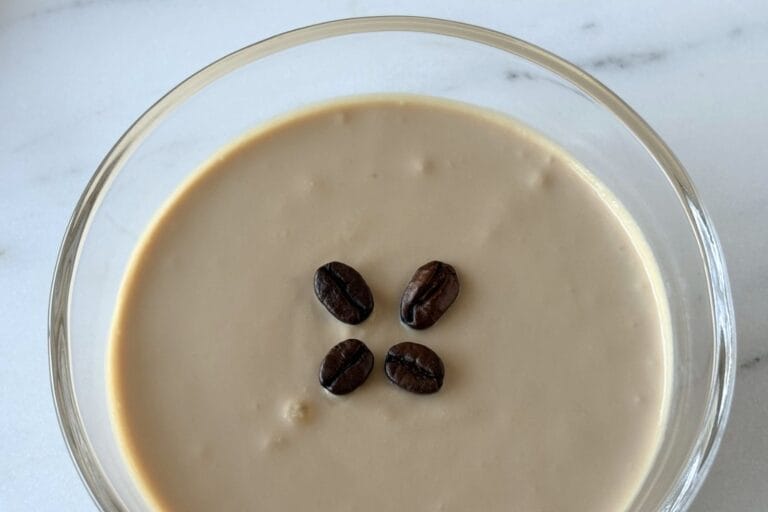 Close-up of ricotta and coffee cream dessert garnished with coffee beans in a shallow glass bowl.