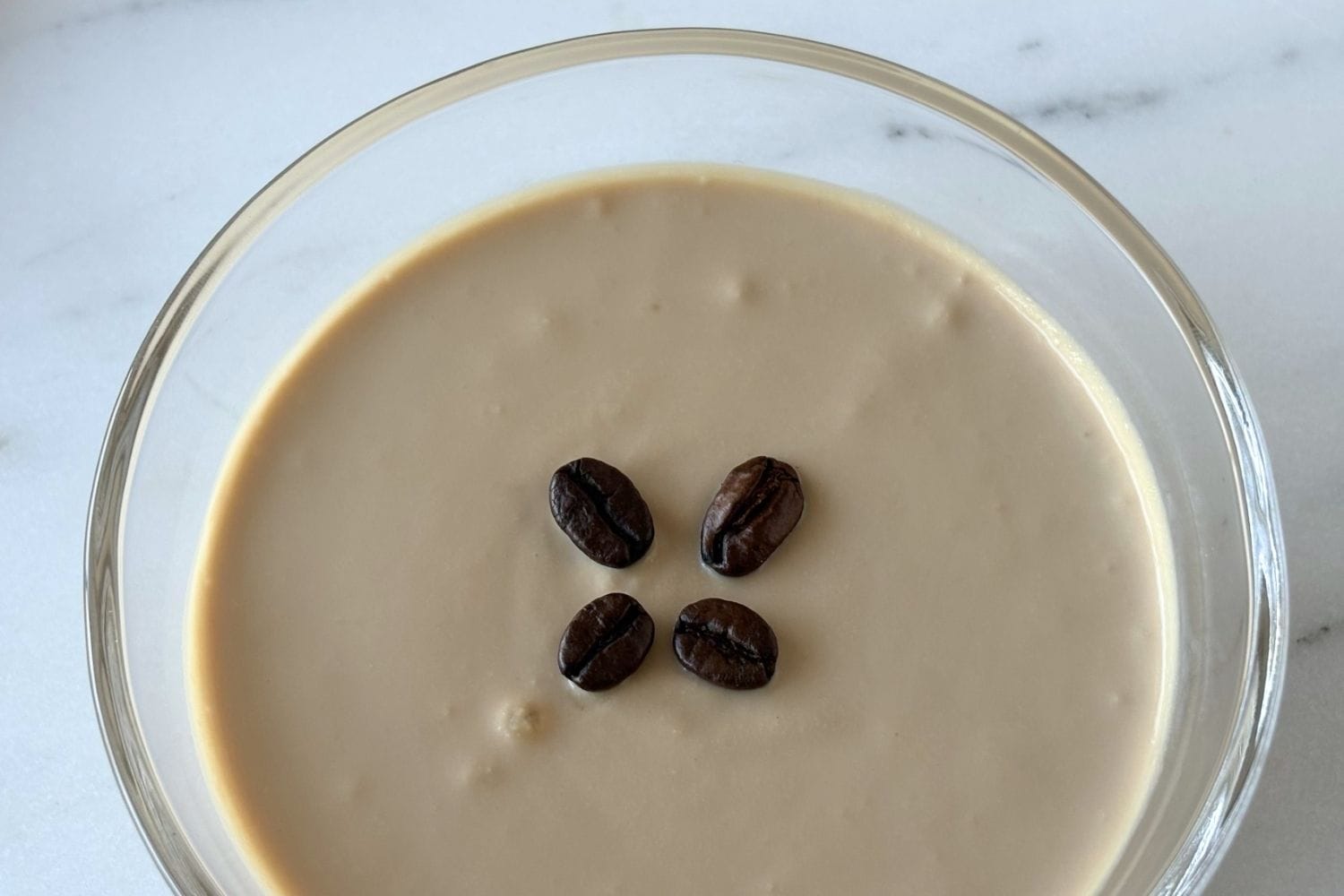 Close-up of ricotta and coffee cream dessert garnished with coffee beans in a shallow glass bowl.