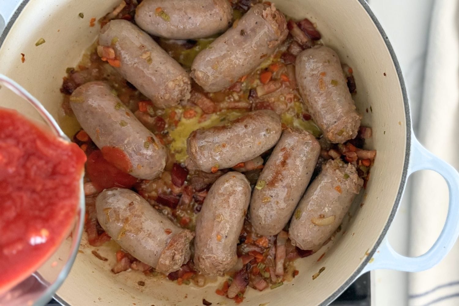 Italian sausages cooking with pancetta and soffritto as tomatoes are added to the pot