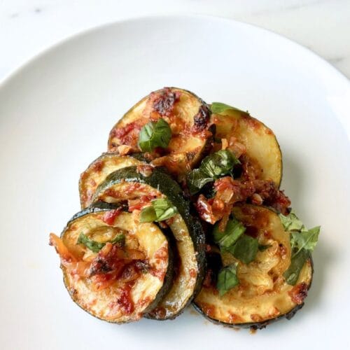 Zucchini with tomato and basil served on a white plate with a light tomato sauce