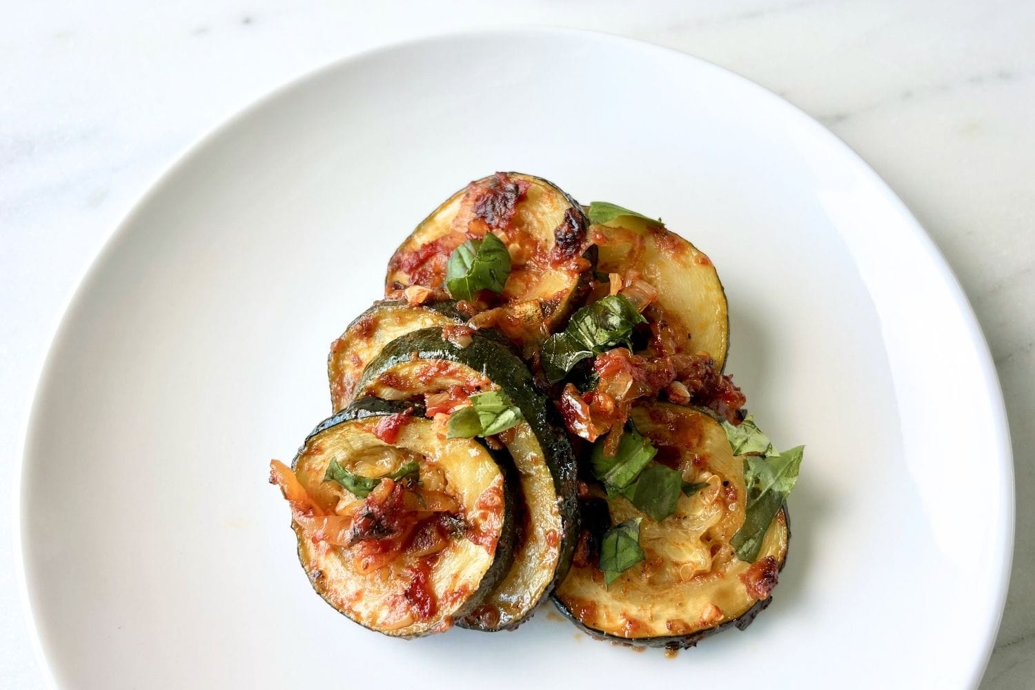 Zucchini with tomato and basil served on a white plate with a light tomato sauce