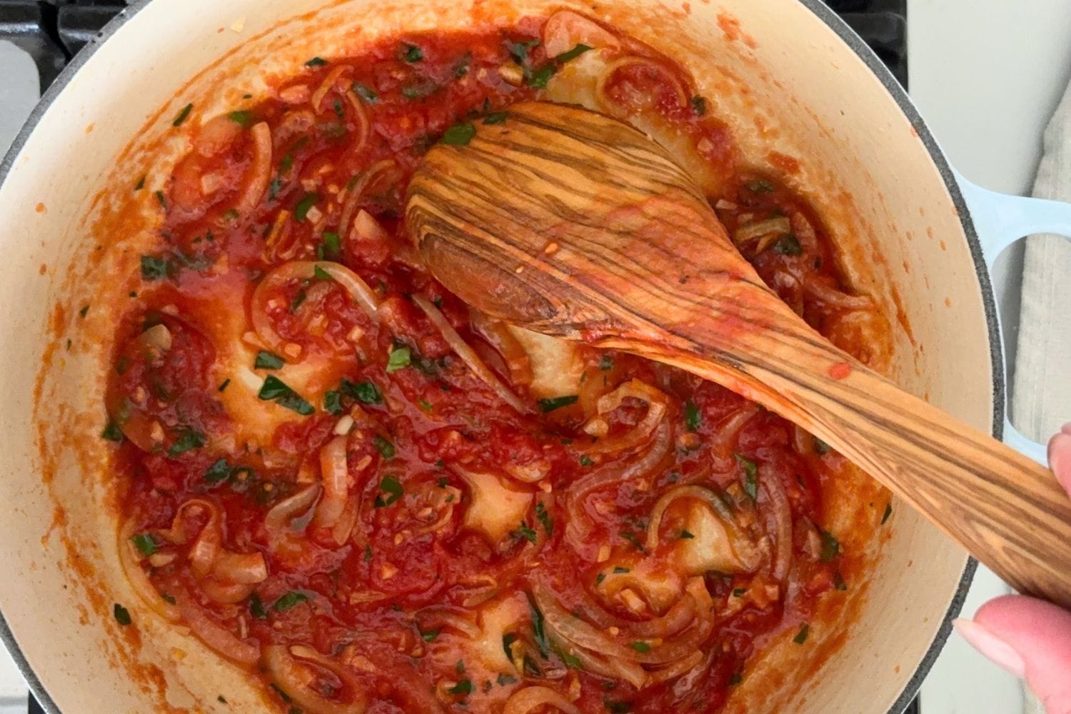 Onion, garlic, and tomatoes simmering in a pot to form the base for zucchini with tomato and basil