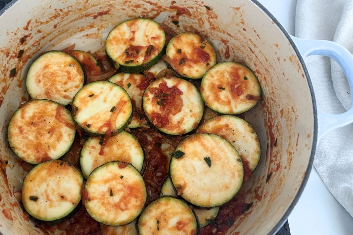 Sliced zucchini layered into a tomato and onion sauce before finishing in the oven