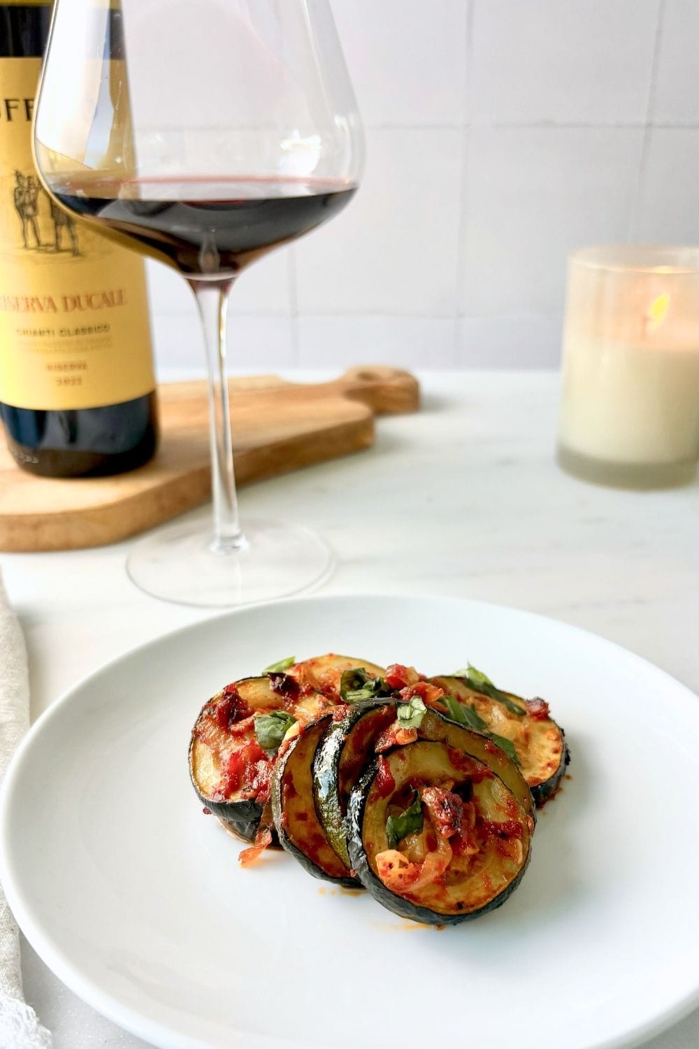 Zucchini with tomato and basil plated with a glass of Chianti and candle in the background