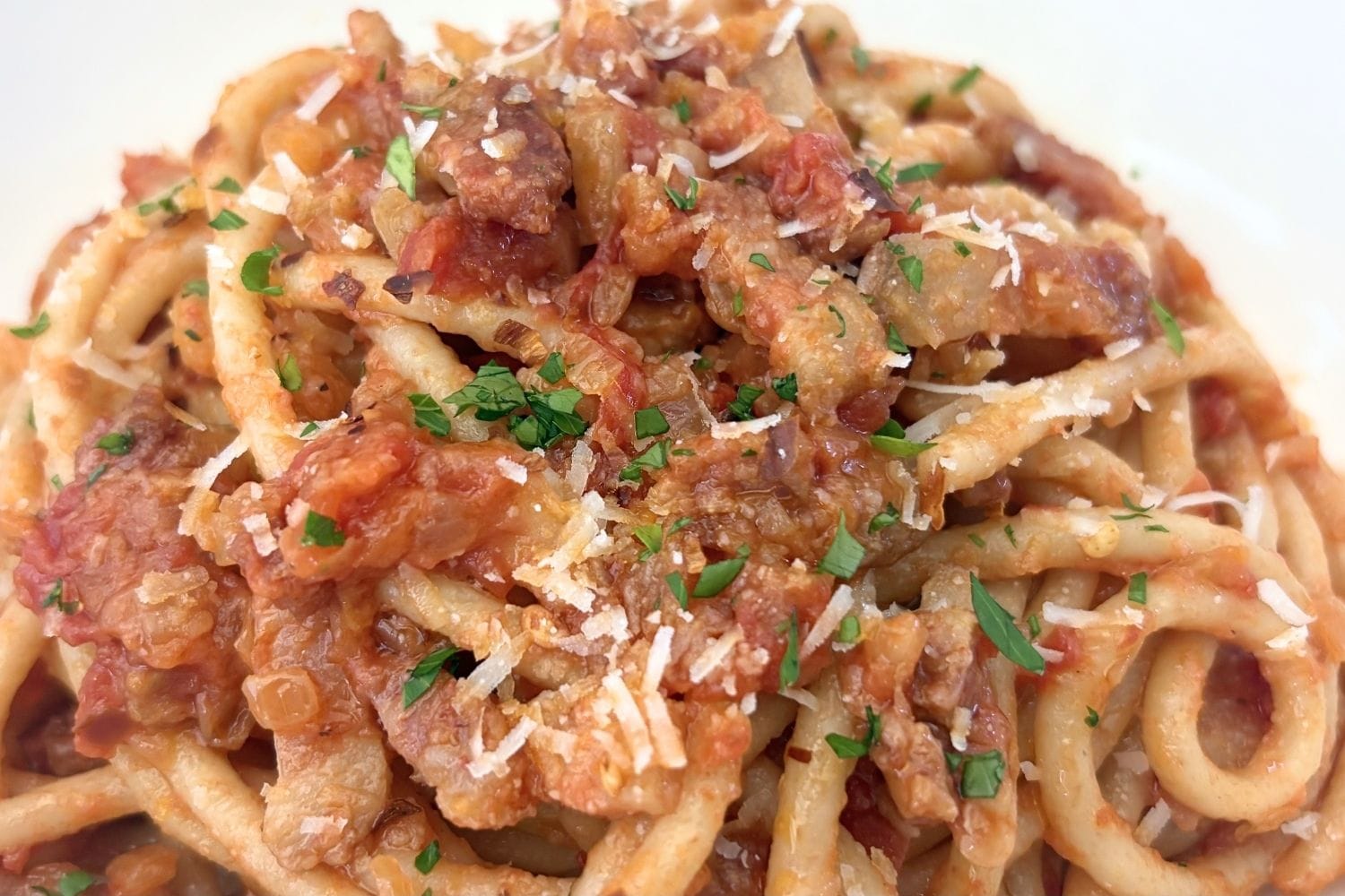 Close-up of Marcella Hazan's Amatriciana sauce with bucatini, pancetta, tomatoes, grated cheese, and parsley.