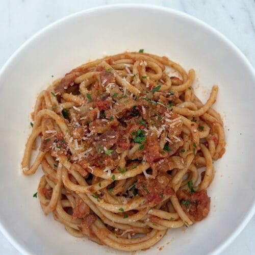 Bowl of bucatini tossed with Amatriciana sauce, pancetta, tomatoes, grated cheese, and parsley.