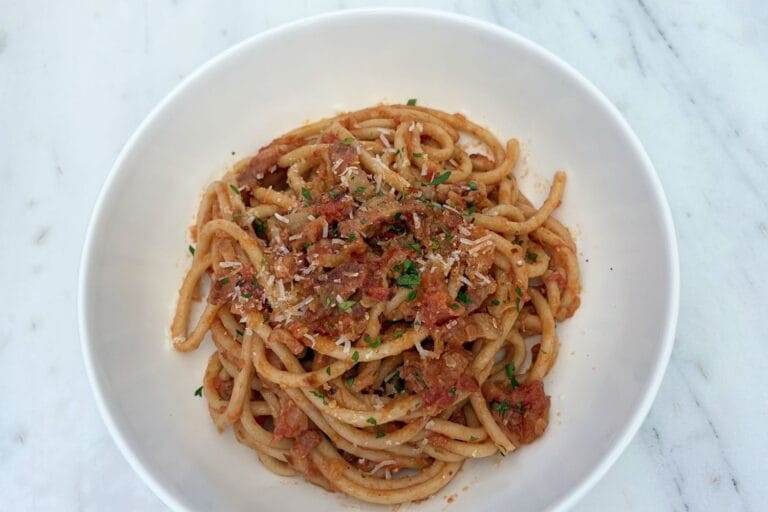 Bowl of bucatini tossed with Amatriciana sauce, pancetta, tomatoes, grated cheese, and parsley.
