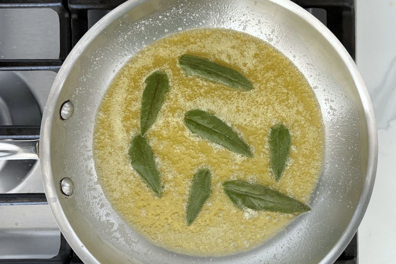 Fresh sage leaves frying in melted butter in a stainless steel skillet, creating the sauce for Marcella Hazan's fettuccine with butter and sage.