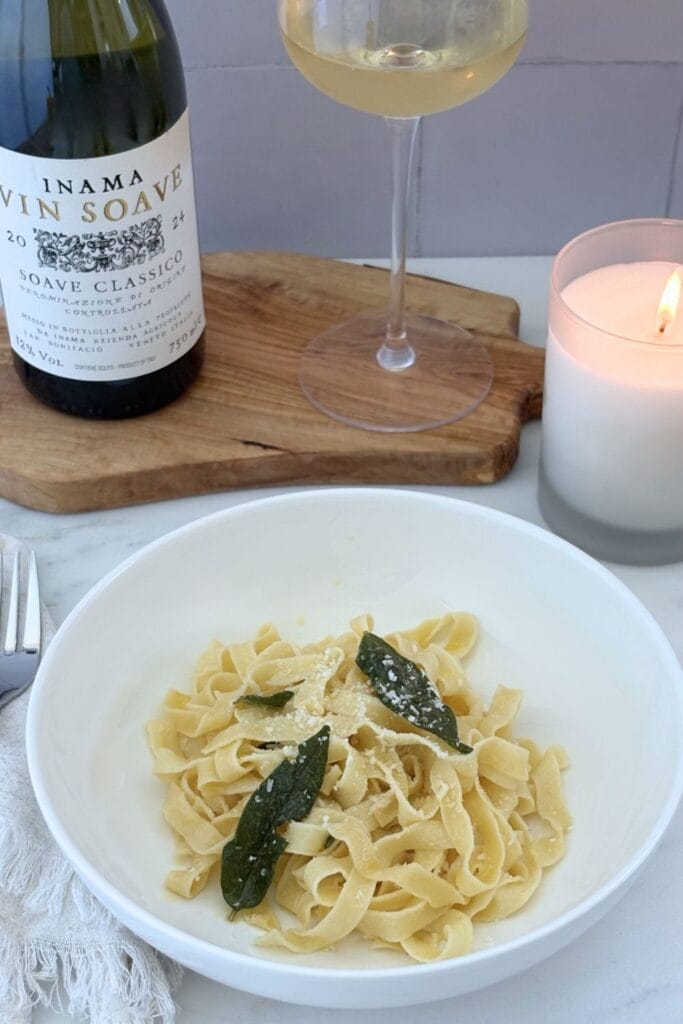Fettuccine with butter and sage sauce served with a glass and bottle of Soave wine and a lit candle.