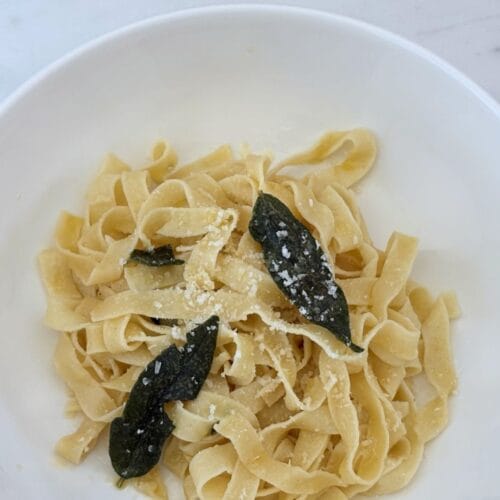 White bowl of fettuccine with butter and fried sage leaves, finished with grated Parmigiano-Reggiano.