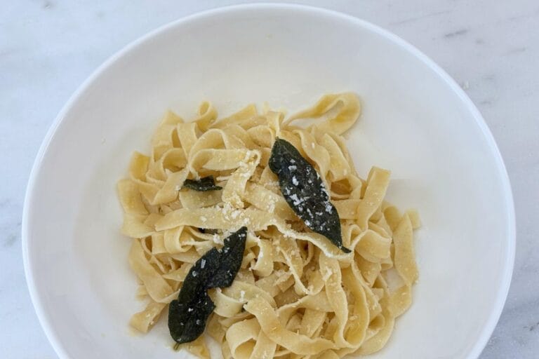 White bowl of fettuccine with butter and fried sage leaves, finished with grated Parmigiano-Reggiano.