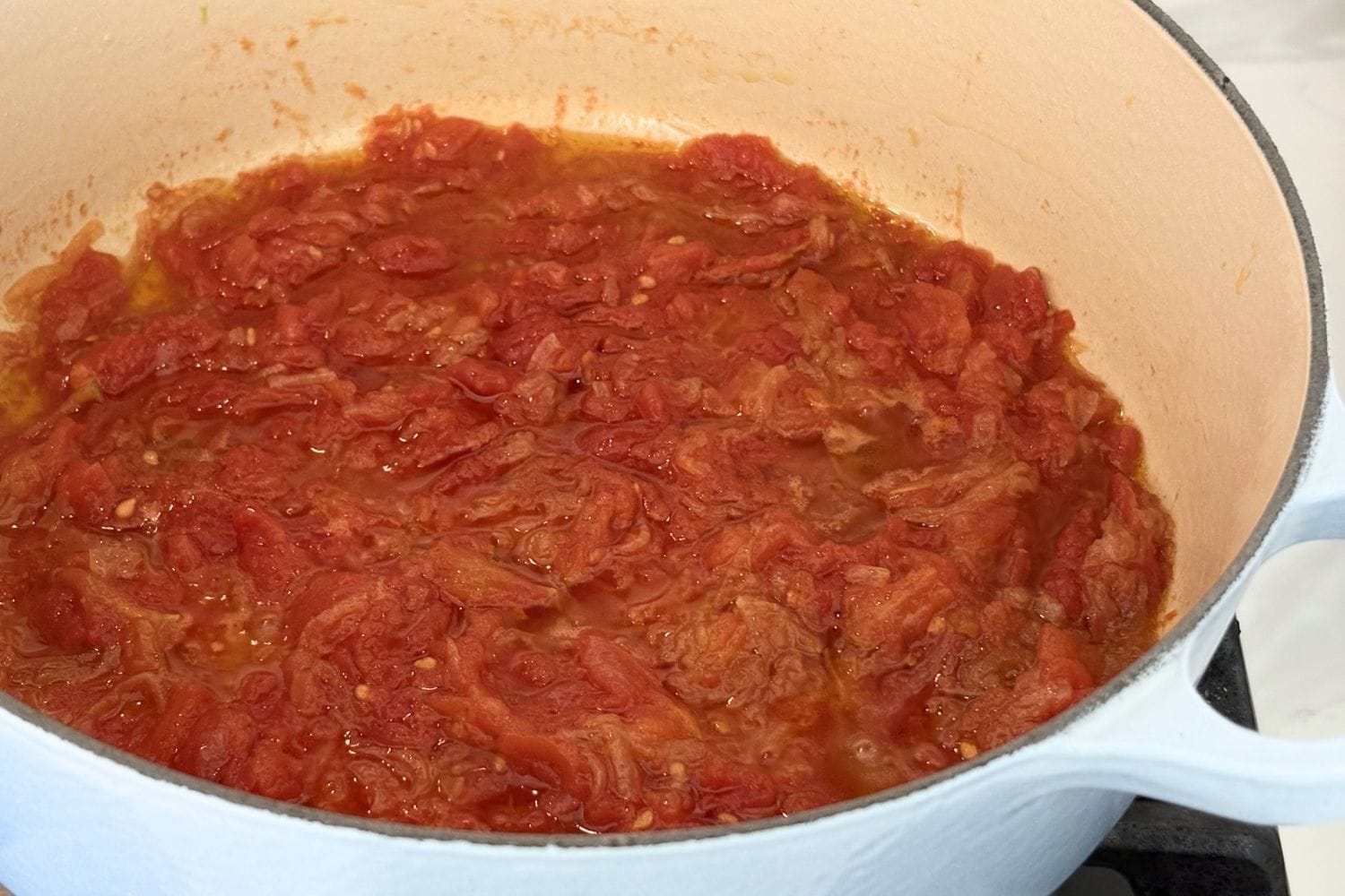 Tomatoes and slowly cooked onions simmering in a white enameled Dutch oven. The mixture has reduced until thick, with olive oil separating slightly around the edges before being added to the eggs for the frittata.