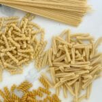 Assorted dried pasta shapes including spaghetti, fusilli, casarecce, and penne arranged on a white marble surface.