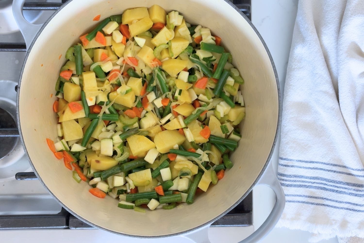 A Dutch oven filled with chopped vegetables including potatoes, green beans, zucchini, carrots, celery, and onions for Marcella Hazan's Minestrone alla Romagnola.