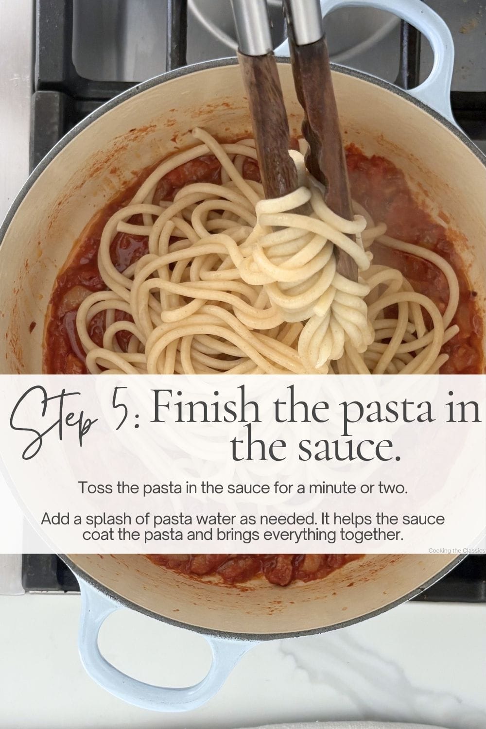 Cooked pasta being tossed into tomato sauce in a Dutch oven using wooden tongs.