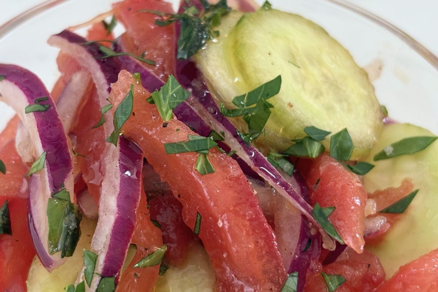 Close-up of Marcella Hazan's tomato, cucumber, onion, and basil salad with peeled tomatoes, thin red onion slices, cucumber rounds, and torn basil dressed with olive oil and vinegar.